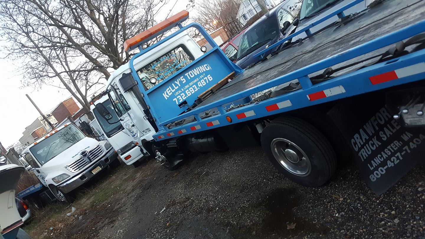 A blue tow truck parked in a lot, showcasing its bright color against the surrounding vehicles and pavement.