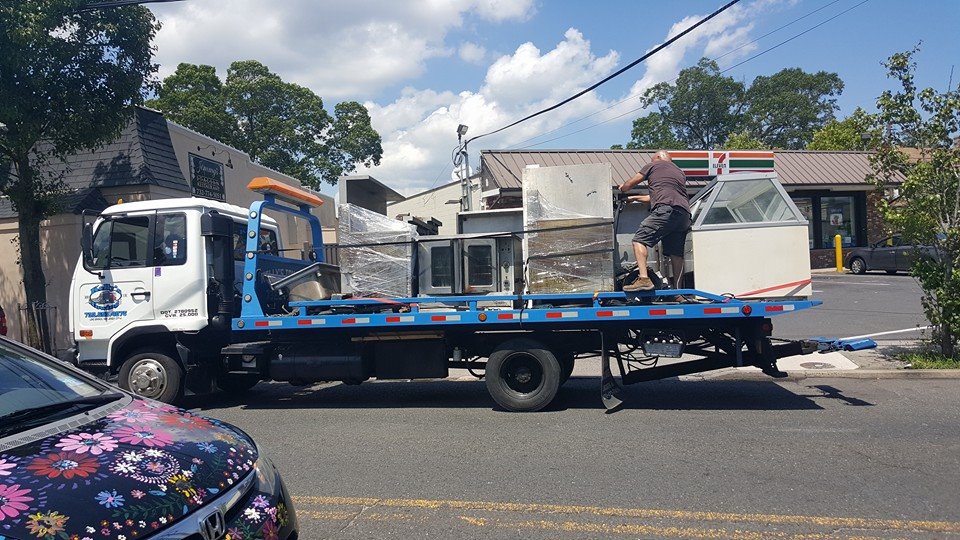 A man is repairing a truck, focused on the engine with tools in hand, surrounded by parts and equipment.