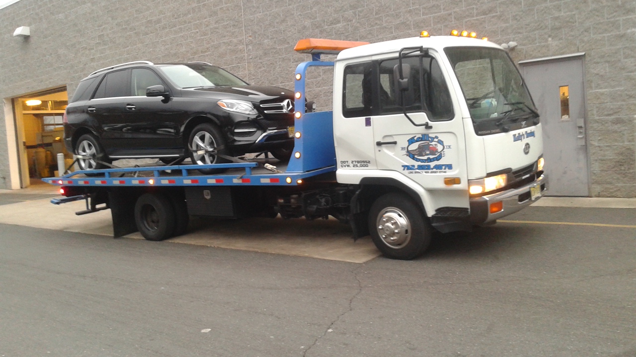 A tow truck carrying a car on its flatbed, parked on the side of the road.