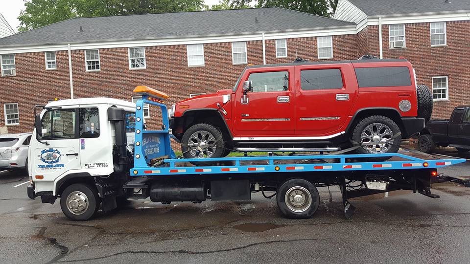 A red jeep is loaded onto a flatbed truck, ready for transport.