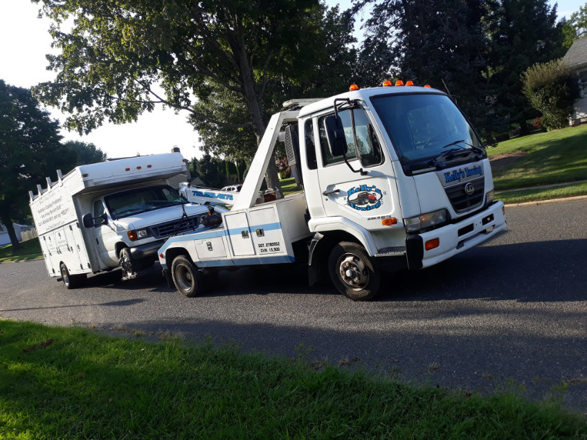 A tow truck is pulling a trailer along the roadside, with clear visibility of the vehicle and surrounding environment.