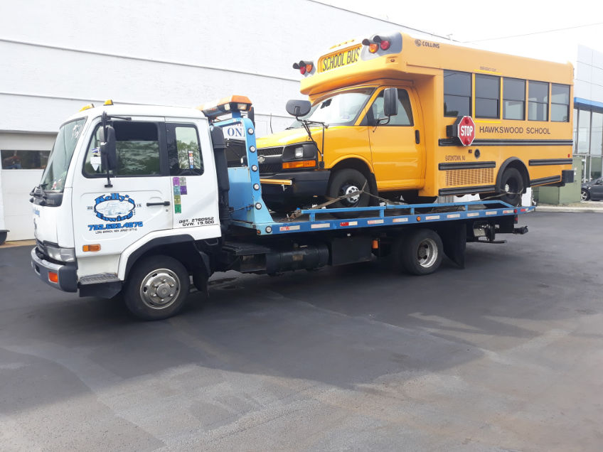 A tow truck is pulling a yellow school bus along the road, indicating a breakdown or transport situation.