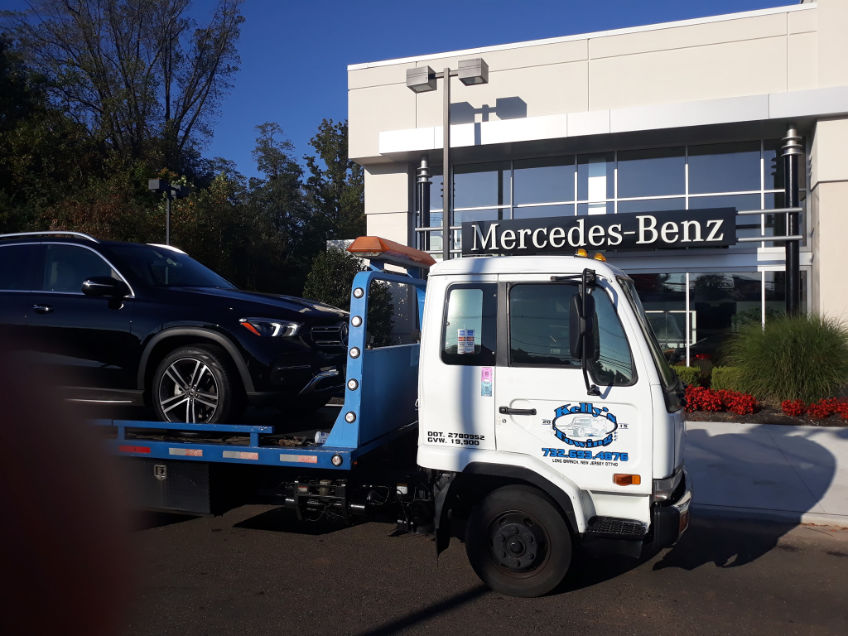 A tow truck parked outside a Mercedes-Benz dealership, ready to assist with vehicle recovery services.