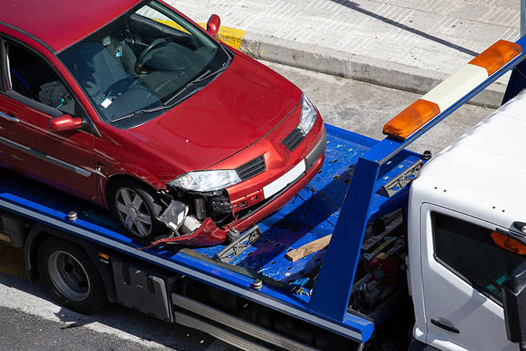 A damaged red car with a crushed front end is being loaded onto a blue tow truck.